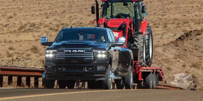RAM pickup truck towing a tractor on a trailer.